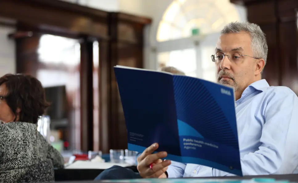 A man sat at a table in BMA House reading a BMA agenda on public health